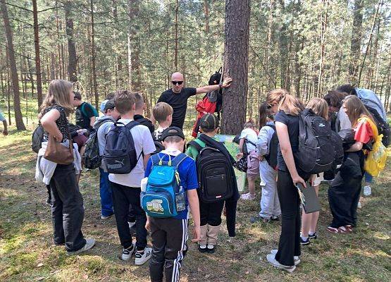 Baza "Orientacja w terenie, węzeł bezpieczeństwa" Grupa dzieci pracuje na stanowisku w środku lasu, uczy się orientować w terenie